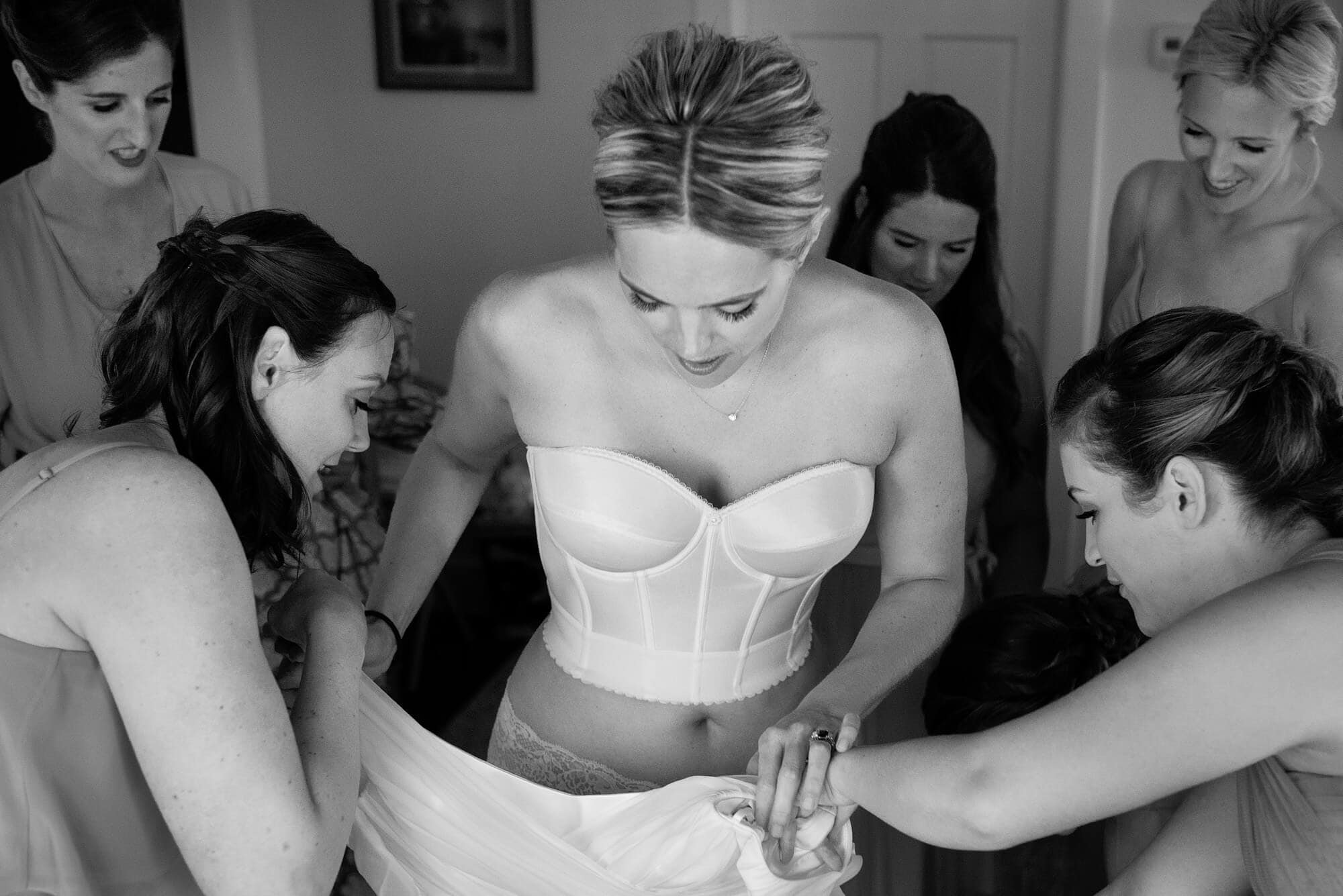 bride in corset getting dressed with all her bridesmaids