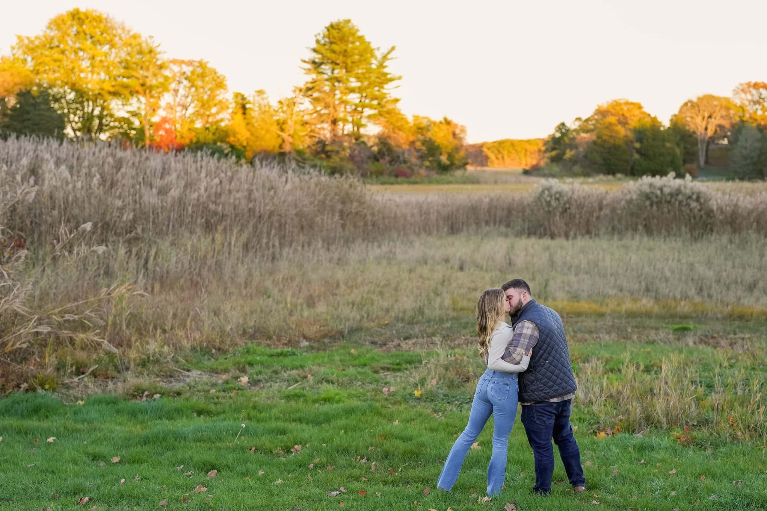 engaged couple kissing in a field in new england in the fall